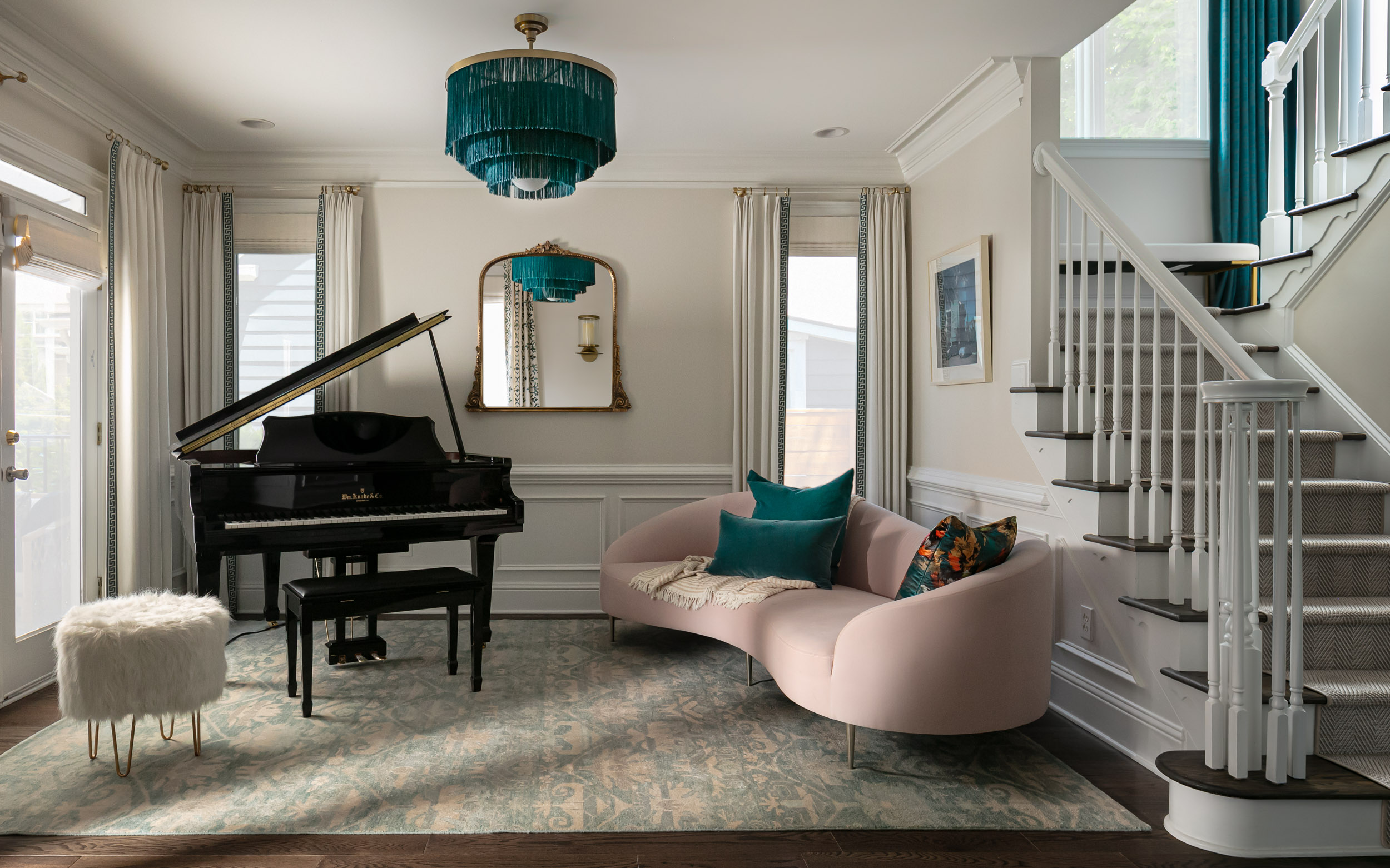 Modern sitting room with piano, chaise, and blue chandelier in front of staircase